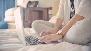 Works and Press Mentions Travel Writing Woman on laptop sitting cross-legged on bed